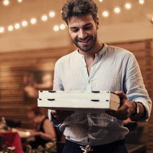 Evening Takeout: Man with Pizzas Exiting Pizzeria Evening Takeout: Man with Pizzas Exiting Pizzeria